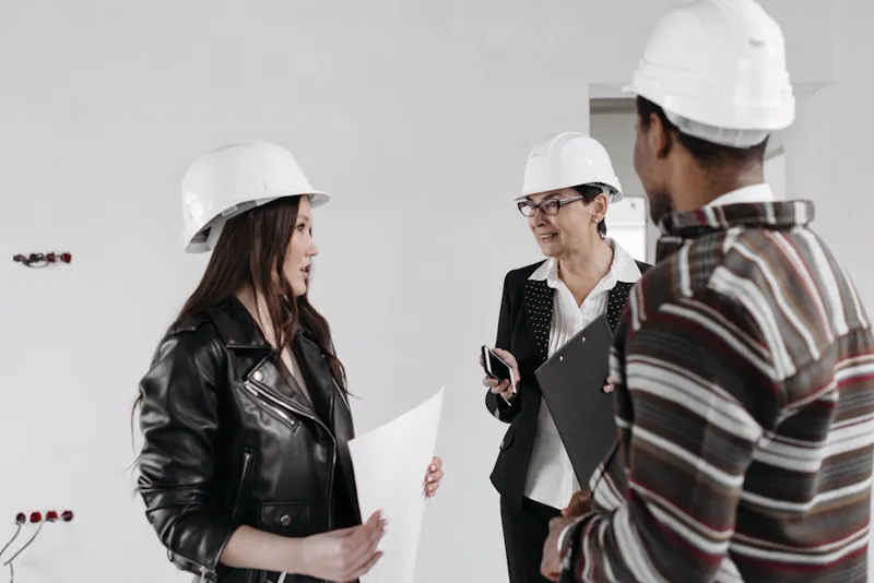 Equipe de arquitetos com capacetes revisando planta técnica dentro do canteiro de obras