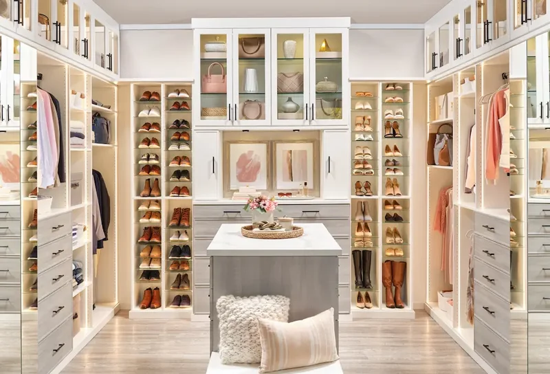 Detalhe da organização interna de um closet, mostrando cabideiros duplos, prateleiras com roupas dobradas e gavetas com divisórias.