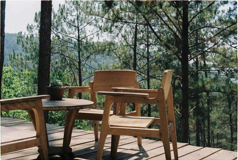 Deck de madeira suspenso em área externa com floresta ao fundo, estrutura de barrotes visível