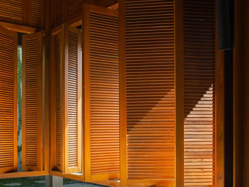 Venezianas de madeira em arquitetura tropical filtrando luz solar e projetando sombras no interior de ambiente residencial