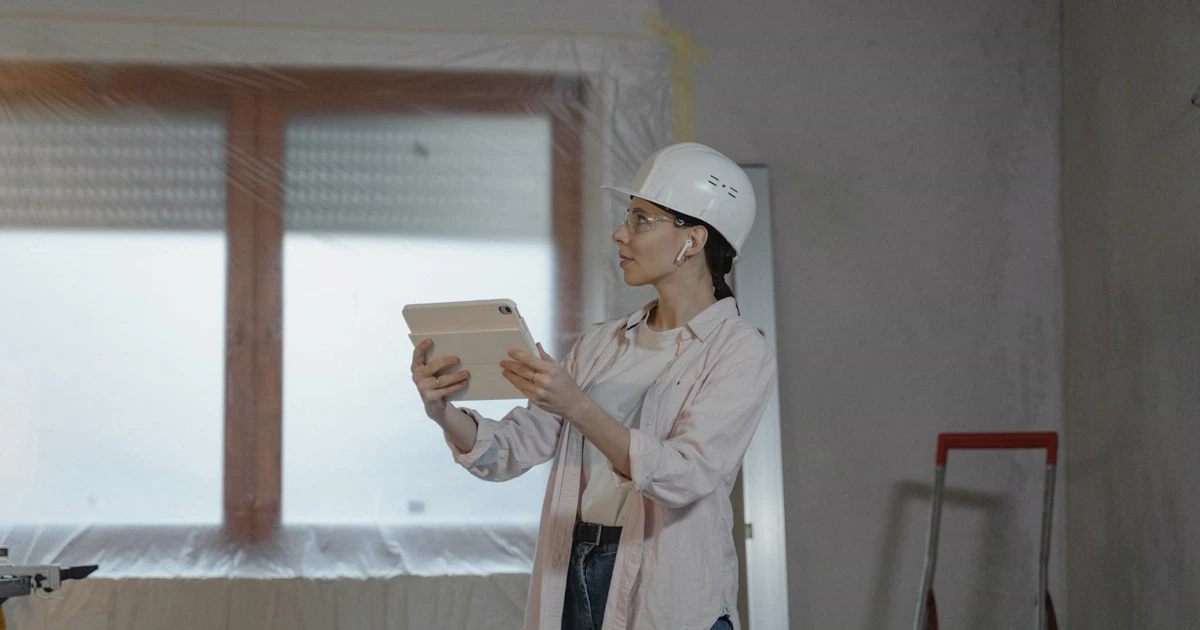 Profissional usando tablet em canteiro de obras para verificar instalações, com planta e modelo 3D em realidade aumentada sobreposto ao ambiente real