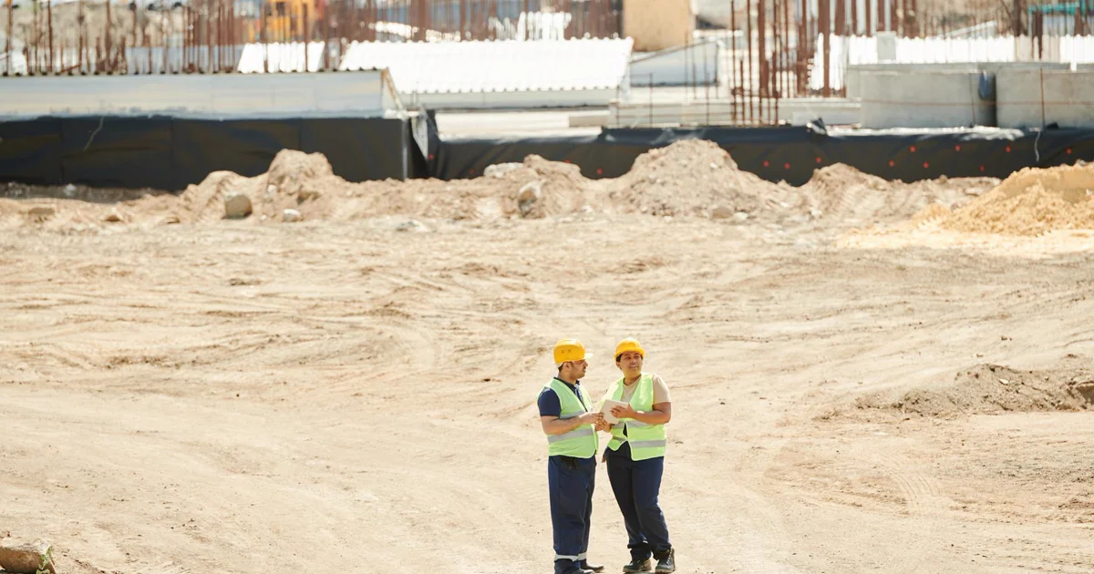 Trabalhador de construção civil verificando documentação técnica em canteiro de obras, representando o uso de RA e BIM para fiscalização e controle de execução