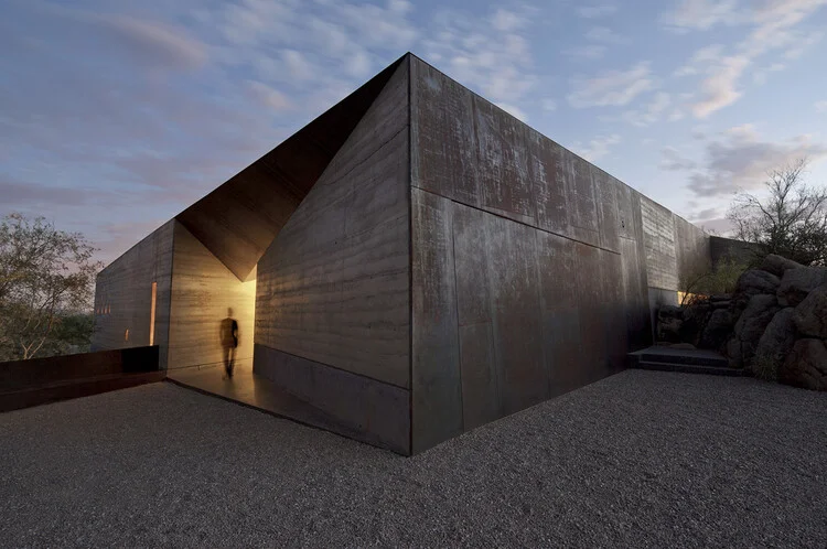 Casa de concreto maciço no deserto ao entardecer — alta massa térmica regulando a temperatura extrema do ambiente árido