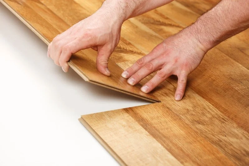 Instalador profissional encaixando uma régua de piso laminado, mostrando o sistema de clique.